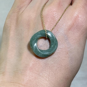 Peut inclure: Un collier pendentif en jade avec un design circulaire torsadé. Le pendentif est de couleur vert sourd et est suspendu à une fine chaîne dorée. Le collier est un bijou.