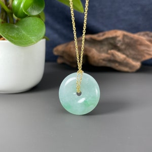May include: A green jade pendant in the shape of a circle with a hole in the center, hanging from a gold chain.