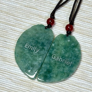 May include: Two green jade heart-shaped pendants with black cords and red beads. The pendants are engraved with the names "Emily" and "Gabriel".