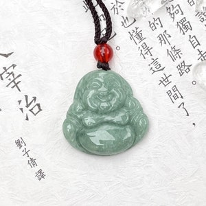 May include: A jade green pendant of a smiling Buddha, with a black cord necklace and a red bead. The pendant is carved in a traditional style, with a rounded body and a serene expression.