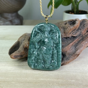 May include: A jade pendant necklace featuring a detailed carving of a Chinese deity. The pendant is a deep green color and is set in a gold tone metal. The necklace is made of a gold tone chain.