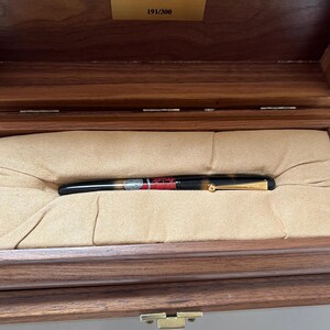 May include: A limited edition White Tiger fountain pen, number 191 of 300, displayed in an open wooden box with a tan interior. The pen is black with gold accents and a detailed design.