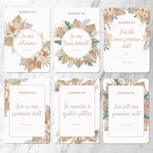 May include: Six printable cards with a neutral color scheme featuring illustrations of pampas grass and flowers. Each card has a different milestone message in French. The messages are 'Je me retourne', 'Je me tiens debout', 'J'ai dit mon premier mot', 'J'ai eu ma premiere dent', 'Je marche a quatre pattes', and 'J'ai fait ma premiere nuit'.