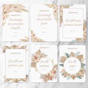 May include: Six printable cards with a neutral color palette featuring illustrations of pampas grass and flowers. Each card has a different message in French, including 'J'ai mangé ma première compote', 'J'ai mangé ma première purée', 'J'ai fait mon premier sourire', 'J'ai fait mes premiers pas', 'J'ai dit maman', and 'J'ai dit papa'. Each card has a space for the date and location.