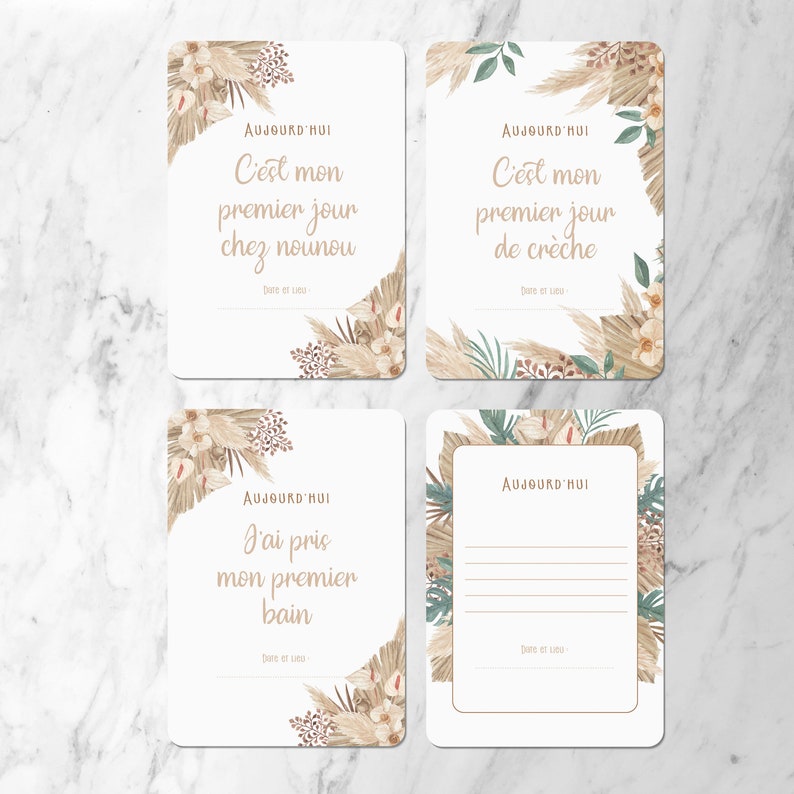 May include: Four printable cards with a neutral color scheme featuring illustrations of pampas grass and other foliage. The cards have the text 'AUJOURD'HUI' and various French phrases including 'C'est mon premier jour chez nounou', 'C'est mon premier jour de crèche', 'J'ai pris mon premier bain', and a blank space for writing. The cards are designed for recording special moments in a baby's life.