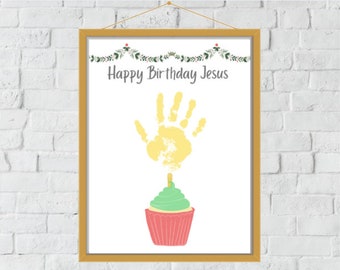 May include: A white framed print with a yellow handprint, a green and pink cupcake, and the text "Happy Birthday Jesus".