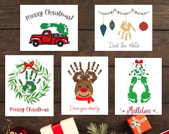 Puede incluir: Cinco tarjetas de Navidad imprimibles con arte de huellas de manos. Las tarjetas presentan un camión rojo con un árbol de huellas de manos verdes, una corona con una huella de manos verdes, un reno con huellas de manos marrones, muérdago con huellas de manos verdes y una guirnalda con un adorno de huellas de manos doradas. Las tarjetas tienen el texto "Feliz Navidad", "Adorna las salas", "Te quiero mi querido reno", "Muérdago", y "Feliz Navidad" en ellas.