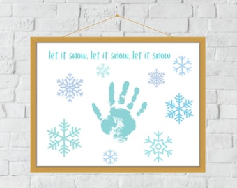 Puede incluir: Una impresión enmarcada en blanco con el texto "let it snow, let it snow, let it snow" y una huella de mano azul rodeada de copos de nieve azules.