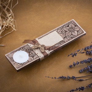 May include: A wooden candle holder with a decorative floral design and a butterfly accent. The holder has a small, round space for a tea light candle.
