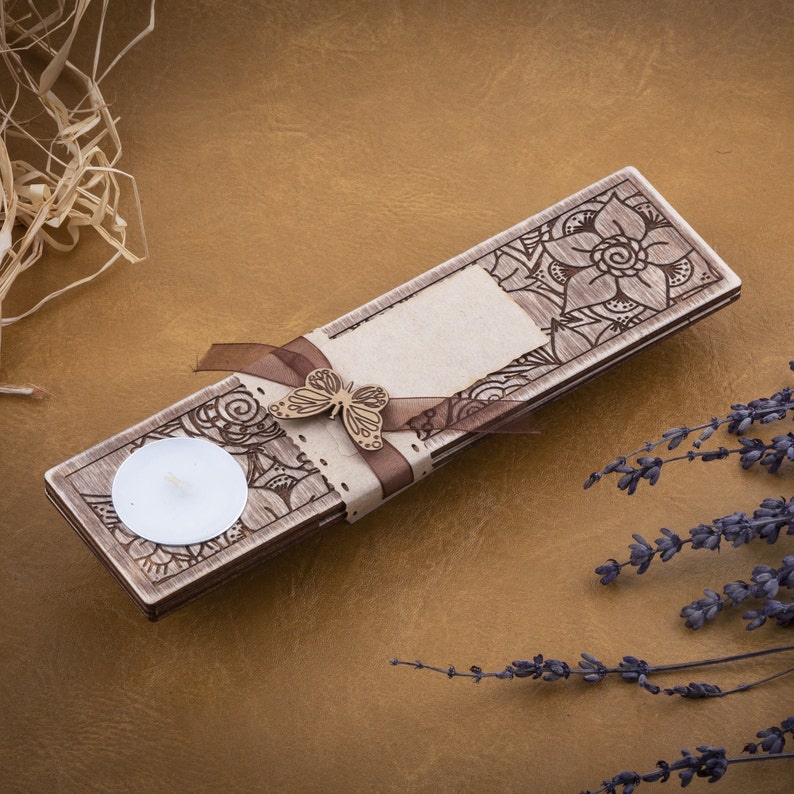 May include: A wooden candle holder with a decorative floral design and a butterfly accent. The holder has a small, round space for a tea light candle.