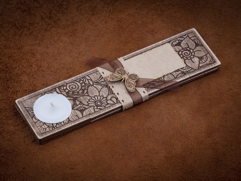 May include: A wooden candle holder with a decorative floral design and a small white candle. The holder has a ribbon tied around it with a butterfly charm.