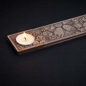 May include: A wooden candle holder with a floral design and a lit tea light candle in the center.