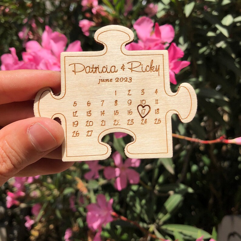 May include: A wooden puzzle piece engraved with "Patricia & Ricky" and "June 2023." The calendar highlights June 17th with a heart. The piece is held against a backdrop of pink flowers.