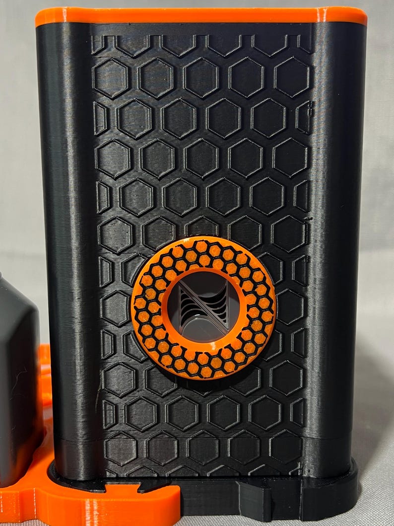 Peut inclure: Un appareil noir et orange imprim&eacute; en 3D avec un motif en nid d'abeille. L'appareil comporte un accent circulaire orange avec un motif g&eacute;om&eacute;trique. Le dessus et la base de l'appareil sont &eacute;galement orange.