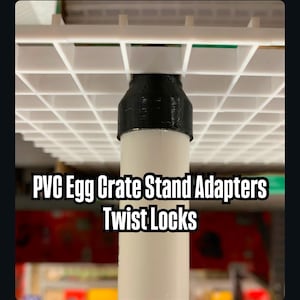 May include: Black plastic adapter for a white PVC pipe. The adapter is designed to connect to a white wire grid shelf. The text "PVC Egg Crate Stand Adapters Twist Locks" is visible below the adapter.