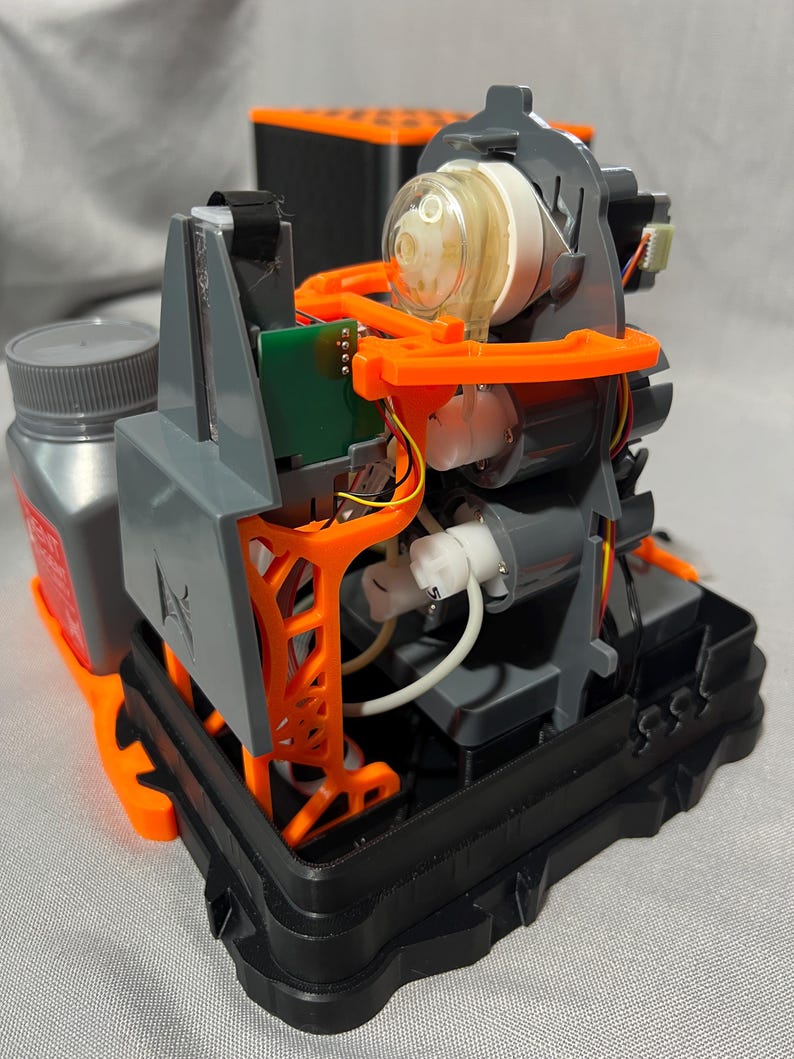 Peut inclure: Un appareil d&eacute;mont&eacute; r&eacute;v&eacute;lant sa structure interne complexe. Il est compos&eacute; de pi&egrave;ces grises, noires et oranges, dont un &eacute;l&eacute;ment cylindrique transparent, une petite carte de circuit imprim&eacute; verte et un flacon gris avec un bouchon gris. Fond gris clair.