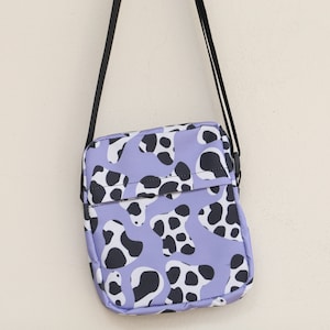 May include: A small purple and black patterned crossbody bag with a black adjustable strap.