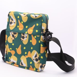 May include: A green crossbody bag with a black adjustable strap. The bag has a zipper closure and a colorful abstract print of yellow and orange shapes.