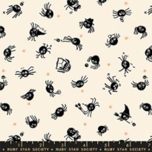 May include: A cream-colored fabric featuring a repeating pattern of small black cartoon spiders in various poses, some wearing hats or holding items, interspersed with tiny orange stars. A black ruler edge is visible at the bottom.