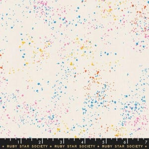 May include: A white fabric with a speckled pattern of blue, pink, yellow, and orange dots. The fabric is a light cream color and the dots are randomly scattered across the surface.