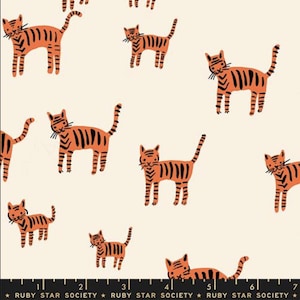 May include: Cream-colored fabric featuring a repeating pattern of orange and black tiger illustrations. The tigers are depicted in various poses, with black stripes and whiskers. The fabric has a playful and whimsical design.