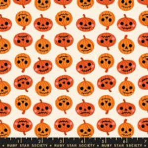 May include: A cream-colored fabric featuring a repeating pattern of orange jack-o'-lanterns with various facial expressions, including smiling and frowning faces. A black measuring tape is visible at the bottom with the text Ruby Star Society.
