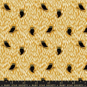 May include: A yellow fabric with a repeating pattern of black owls with yellow eyes on white branches. The fabric has a white and yellow feather pattern in the background. The fabric is marked with a ruler in inches.