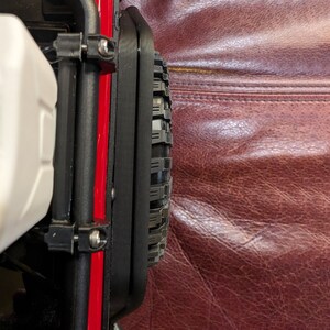 Puede incluir: Un protector de guardabarros de pl&aacute;stico negro montado en un chasis de veh&iacute;culo rojo, con un acabado texturizado y fijado con tornillos met&aacute;licos visibles. El componente est&aacute; colocado junto a un neum&aacute;tico de goma negro con banda de rodadura.