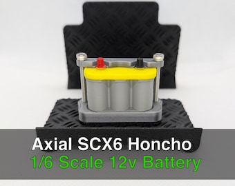 Puede incluir: Modelo de batería de 12V a escala 1/6 para Axial SCX6 Honcho. La batería es gris con una parte superior amarilla y terminales rojos y negros. El modelo está montado sobre una base de chapa de diamante negra.