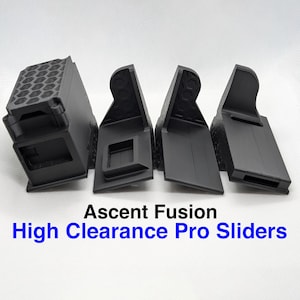 May include: Four black Ascent Fusion High Clearance Pro Sliders are displayed against a white background. The sliders are made of a textured material and have various geometric shapes and cutouts. The text "Ascent Fusion" and "High Clearance Pro Sliders" is visible.