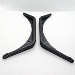 Puede incluir: Un par de soportes en L negros impresos en 3D con un dise&ntilde;o curvo. Cada soporte tiene un acabado de superficie texturizado e incluye dos orificios de montaje circulares colocados a lo largo del marco para una fijaci&oacute;n segura.