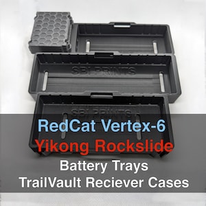 May include: Black plastic battery trays and receiver cases, including a RedCat Vertex-6 and Yikong Rockslide model. The trays are rectangular with slots and the cases have lids. The text "SBI PRINTS" is visible on the trays.