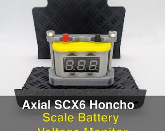 Pode incluir: Um monitor de tensão de bateria em escala para Axial SCX6 Honcho. O dispositivo tem um corpo cinza com uma parte superior amarela e um visor digital que mostra a tensão. O monitor tem terminais vermelhos e pretos e é montado em uma base de chapa de diamante preta.