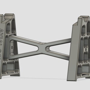 May include: A gray metal stand with a triangular design and the text "AXIAL SCX6" printed on one side. The stand is designed to hold a model car.