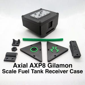 Pode incluir: Uma caixa de receptor de tanque de combustível em escala Axial AXP8 Gilamon preta com peças verdes e pretas. A caixa tem uma tampa superior com um painel prateado e uma mangueira verde.