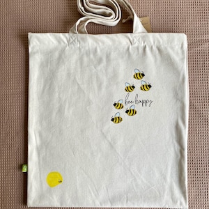 May include: A white canvas tote bag with a yellow bee design and the text "bee happy".