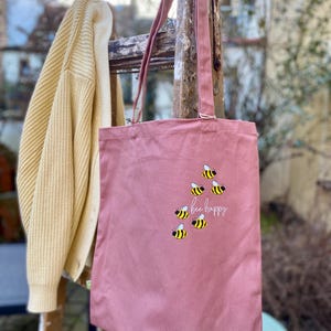 May include: A pink canvas tote bag with the text "bee happy" and a design of yellow and black bees.