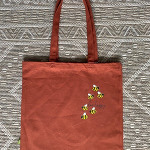 May include: A brown canvas tote bag with the text "bee happy" and a design of bees in yellow and black.