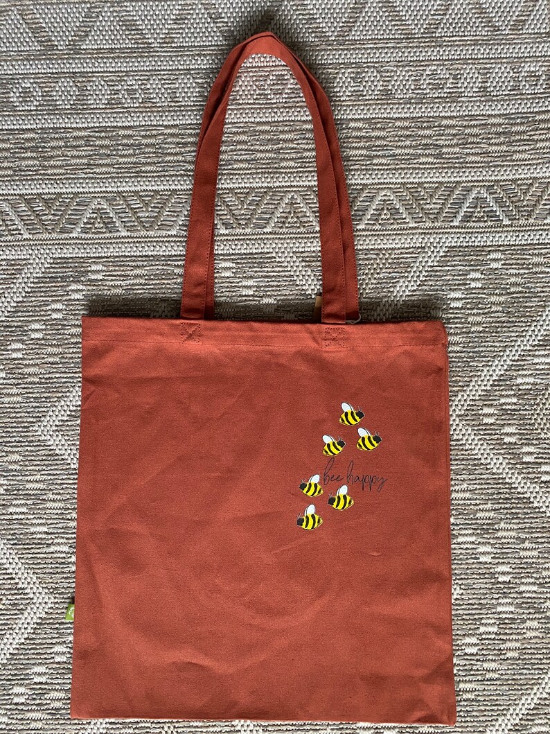 May include: A brown canvas tote bag with the text "bee happy" and a design of bees in yellow and black.
