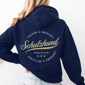 May include: Navy blue hoodie with a gold-colored Schutzhund design on the back. The design includes the word "Schutzhund" in a script font, surrounded by the words "Tracking, Obedience, Working Dog, Protection, Endurance."