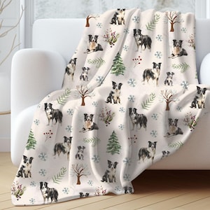 May include: A white fleece throw blanket with a repeating pattern of black and white border collies, snowflakes, pine trees, and red berries.