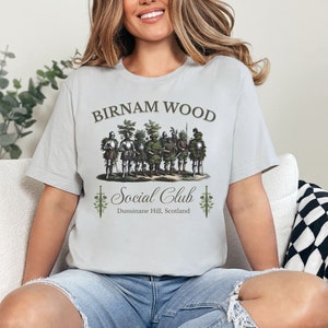 May include: A gray t-shirt with the text "Birnam Wood Social Club" and a graphic of a group of men in armor with trees growing out of their helmets. The text "Dunsinane Hill, Scotland" is below the graphic.