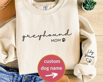 May include: A cream colored sweatshirt with the text "greyhound MOM" and a paw print. The sleeve has a heart with a paw print and the text "Lily Boomer".