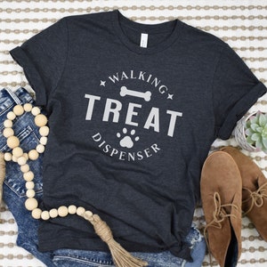 May include: A dark grey t-shirt with a white graphic that says "Walking Treat Dispenser" with a bone and paw print.