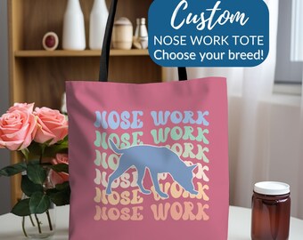 May include: Pink tote bag with a blue silhouette of a dog sniffing the ground. The bag has the text "Nose Work" repeated in rainbow colors.