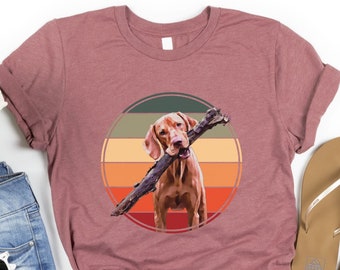 May include: A heather mauve t-shirt featuring a retro-style graphic of a brown dog holding a stick in its mouth. The graphic is set against a circular background with orange, yellow, and green stripes.
