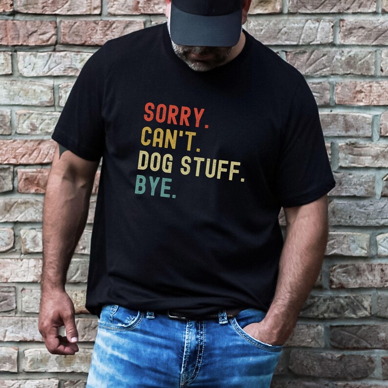 以下が含まれることがあります： レトロなフォントでカラフルなアクセントがついた「SORRY. CAN'T. DOG STUFF. BYE.」というテキストが書かれた黒いTシャツです。