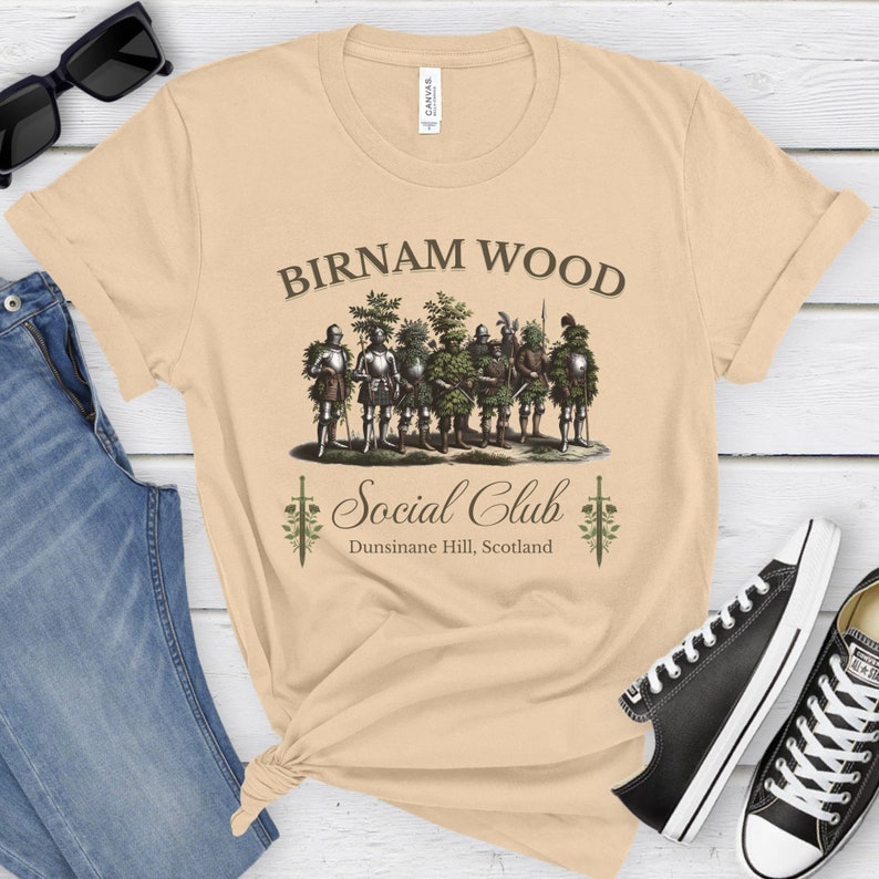 May include: A beige t-shirt with a graphic of a group of men dressed as trees, with the text "Birnam Wood Social Club Dunsinane Hill, Scotland".