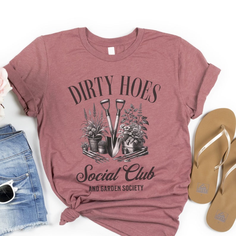 May include: A maroon t-shirt with the text "Dirty Hoes Social Club and Garden Society" in black lettering. A vintage illustration of gardening tools and plants is featured above the text.