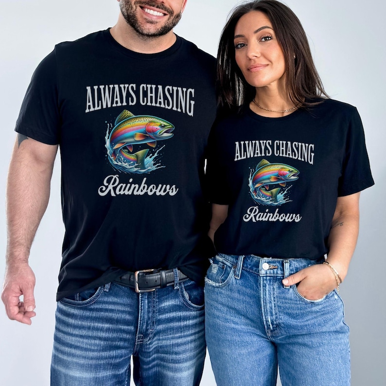 May include: Two black t-shirts with the text "Always Chasing Rainbows" and a rainbow trout graphic. The shirts are worn by two people.